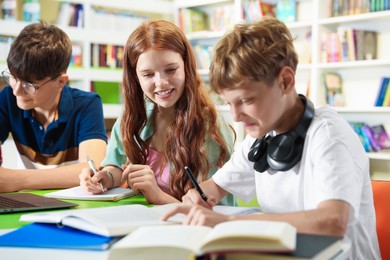 Photo of Students with books studying together at table in library