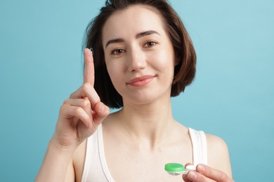 Photo of Woman with contact lens and case on light blue background