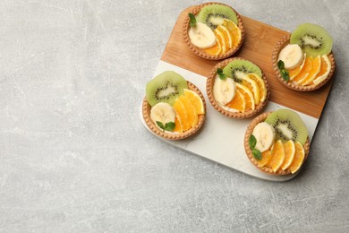 Photo of Delicious dessert. Tartlets with fruits and mint on gray textured table, top view. Space for text