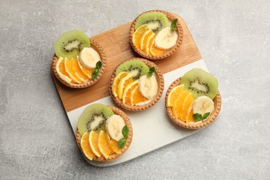 Photo of Tartlets with fruits and mint on gray textured table, top view. Delicious dessert