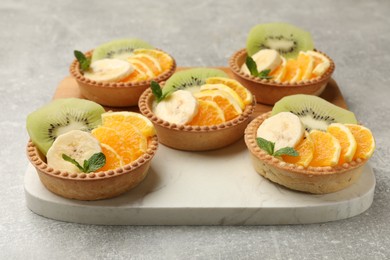 Photo of Tartlets with fruits and mint on gray textured table, closeup. Delicious dessert