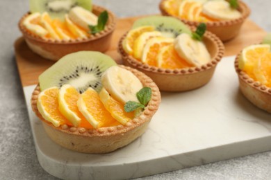 Photo of Tartlets with fruits and mint on gray textured table, closeup. Delicious dessert