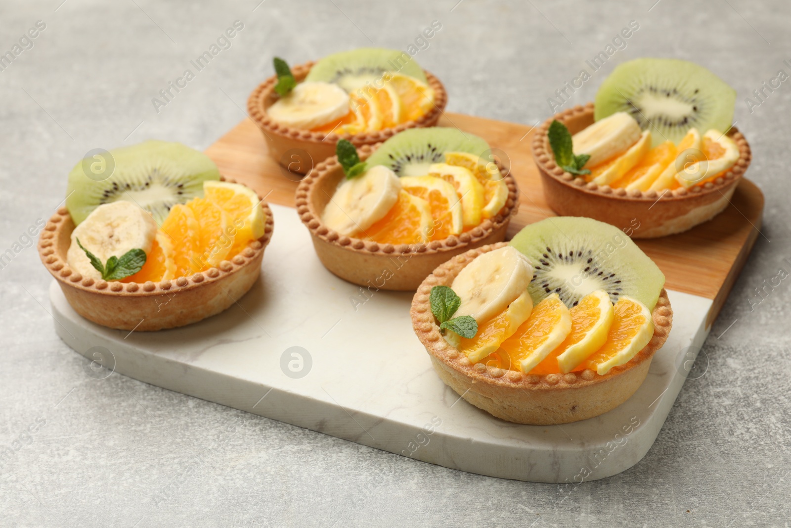 Tartlets with fruits and mint on gray textured table, closeup. Delicious dessert Photo of Tartlets with fruits and mint on gray textured table, closeup. Delicious dessert