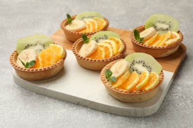 Photo of Tartlets with fruits and mint on gray textured table, closeup. Delicious dessert