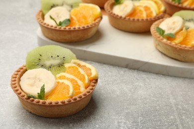 Photo of Tartlets with fruits and mint on gray textured table, closeup. Delicious dessert