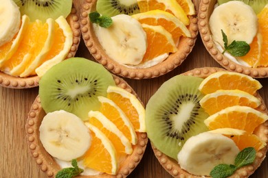 Photo of Tartlets with fruits and mint on table, top view. Delicious dessert