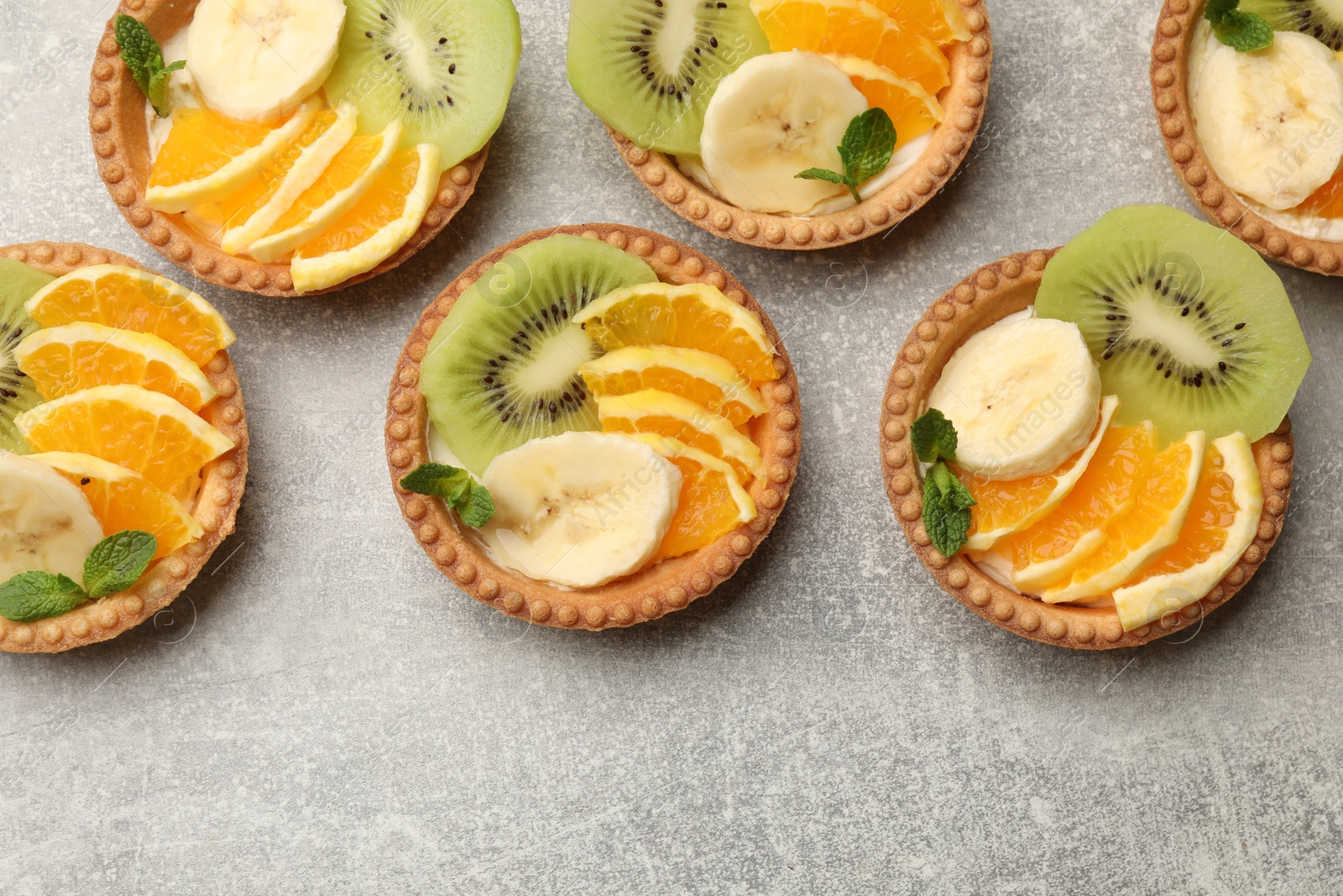 Tartlets with fruits and mint on gray textured table, flat lay. Delicious dessert Photo of Tartlets with fruits and mint on gray textured table, flat lay. Delicious dessert