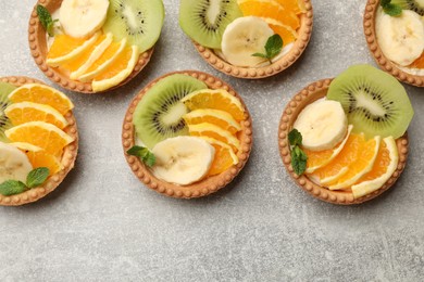 Photo of Tartlets with fruits and mint on gray textured table, flat lay. Delicious dessert