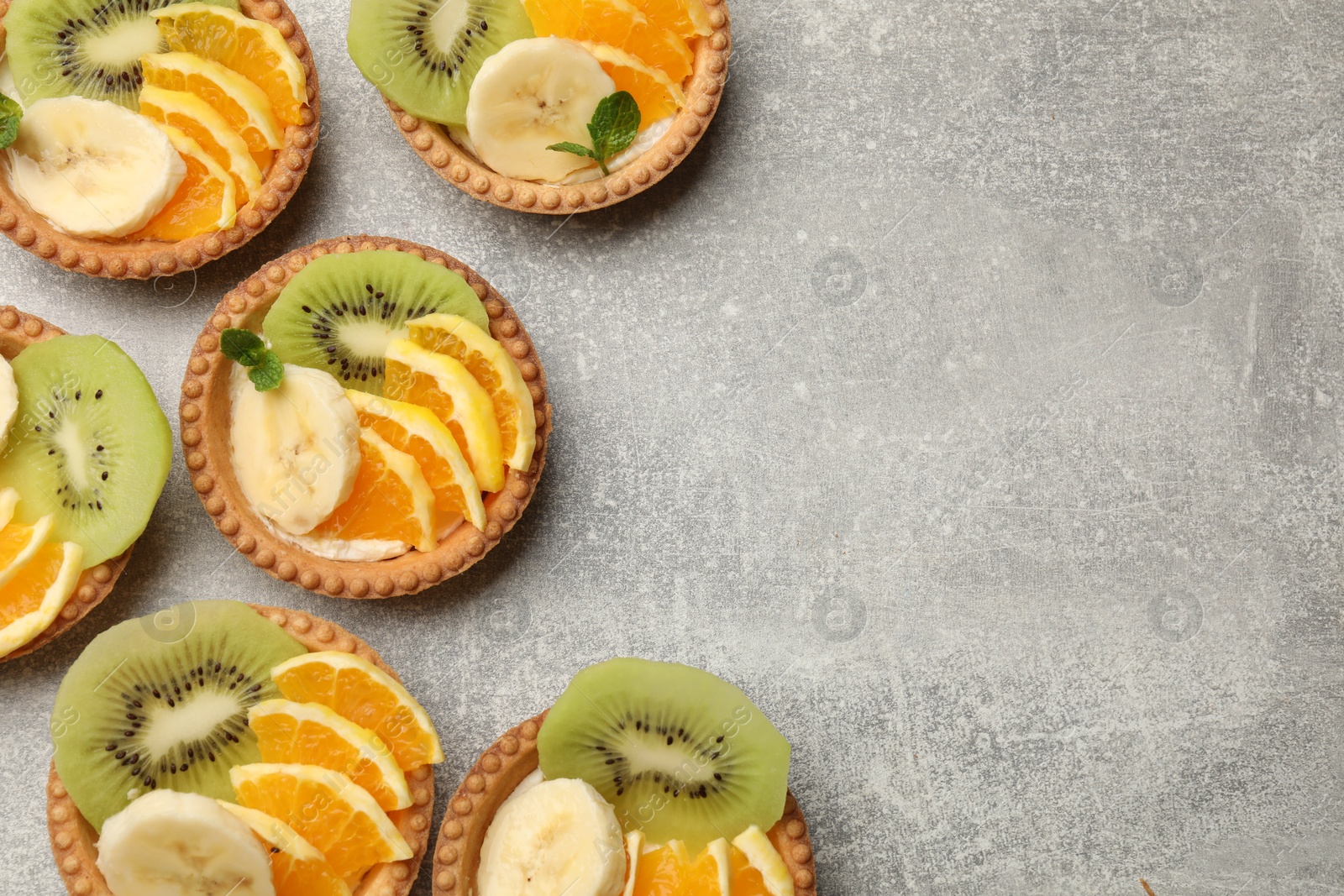 Delicious dessert. Tartlets with fruits and mint on gray textured table, flat lay. Space for text Photo of Delicious dessert. Tartlets with fruits and mint on gray textured table, flat lay. Space for text