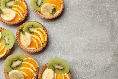 Photo of Delicious dessert. Tartlets with fruits and mint on gray textured table, flat lay. Space for text