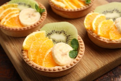 Photo of Tartlets with fruits and mint on table, closeup. Delicious dessert