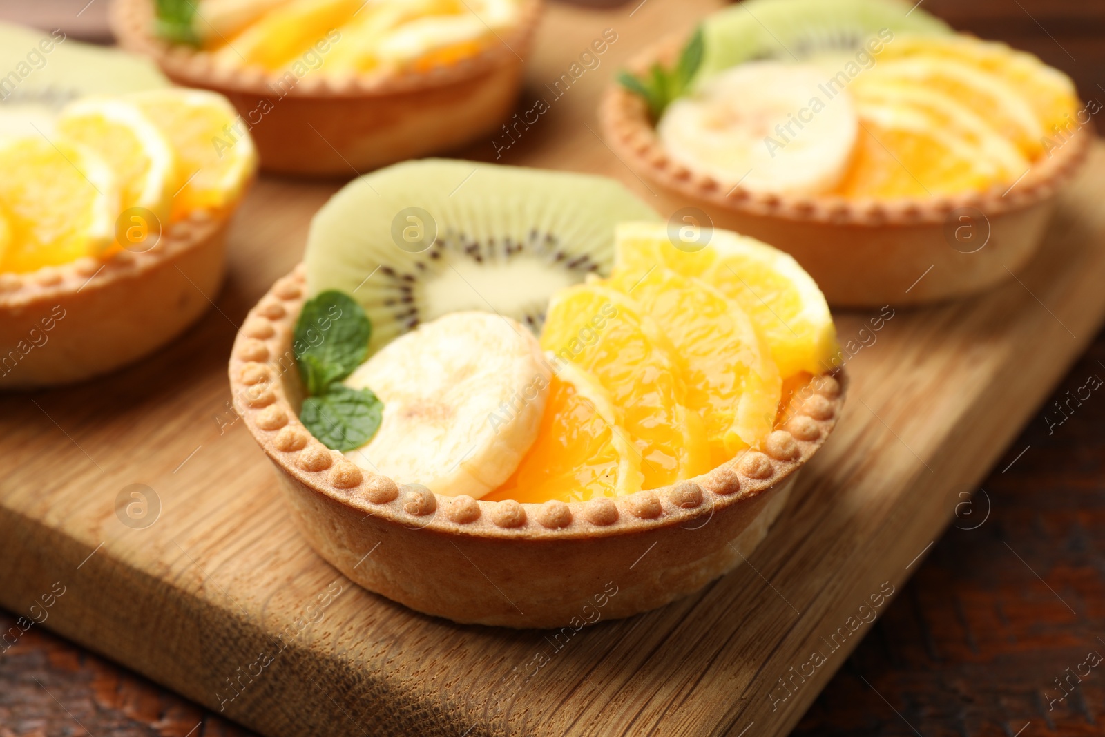 Tartlets with fruits and mint on table, closeup. Delicious dessert Photo of Tartlets with fruits and mint on table, closeup. Delicious dessert