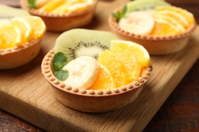 Photo of Tartlets with fruits and mint on table, closeup. Delicious dessert