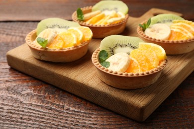 Photo of Tartlets with fruits and mint on wooden table, closeup. Delicious dessert