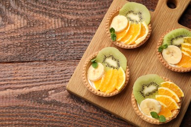 Photo of Delicious dessert. Tartlets with fruits and mint on wooden table, top view. Space for text