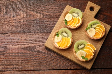 Photo of Delicious dessert. Tartlets with fruits and mint on wooden table, top view. Space for text