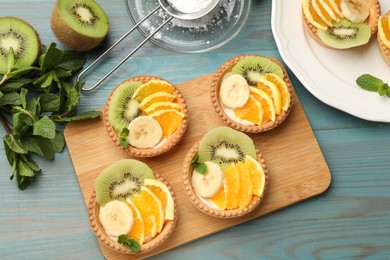 Photo of Tartlets with fruits and mint on light blue wooden table, flat lay. Delicious dessert