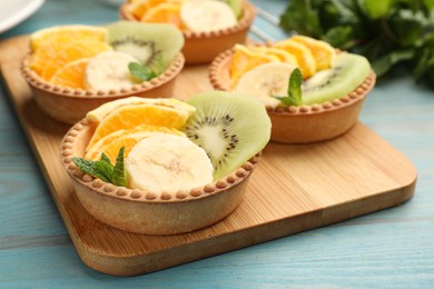 Photo of Tartlets with fruits and mint on light blue wooden table, closeup. Delicious dessert