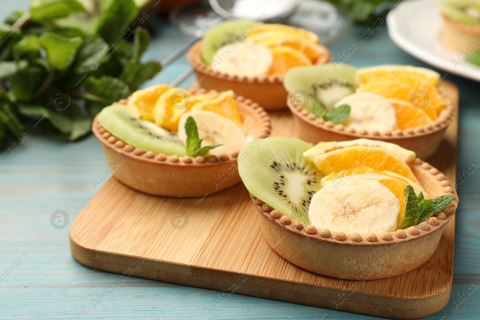 Tartlets with fruits and mint on light blue wooden table, closeup. Delicious dessert Photo of Tartlets with fruits and mint on light blue wooden table, closeup. Delicious dessert