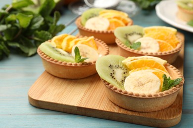 Photo of Tartlets with fruits and mint on light blue wooden table, closeup. Delicious dessert