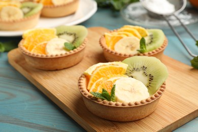 Photo of Tartlets with fruits and mint on light blue wooden table, closeup. Delicious dessert