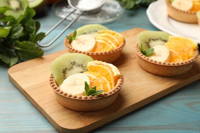 Photo of Tartlets with fruits and mint on light blue wooden table, closeup. Delicious dessert