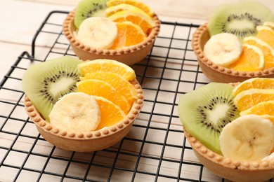Photo of Tartlets with fruits on wooden table, closeup. Delicious dessert