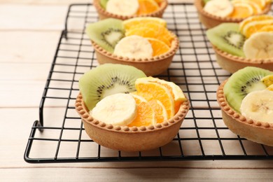 Photo of Tartlets with fruits on wooden table, closeup. Delicious dessert