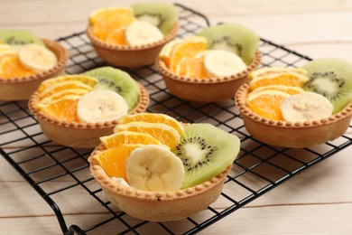 Photo of Tartlets with fruits on wooden table, closeup. Delicious dessert