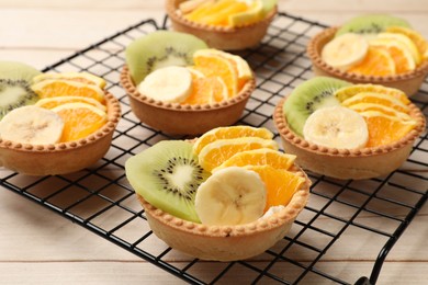 Photo of Tartlets with fruits on wooden table, closeup. Delicious dessert