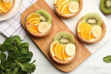 Photo of Tartlets with fruits and mint on white table, flat lay. Delicious dessert