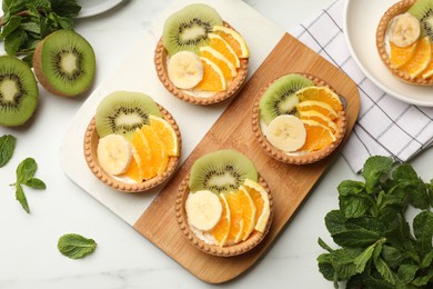 Photo of Tartlets with fruits and mint on white table, flat lay. Delicious dessert