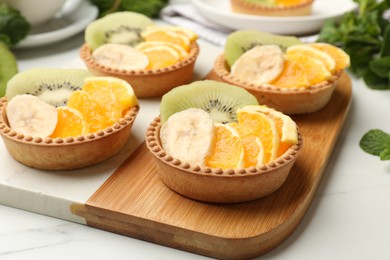 Photo of Tartlets with fruits and mint on white table, closeup. Delicious dessert