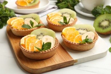 Photo of Tartlets with fruits and mint on white table, closeup. Delicious dessert