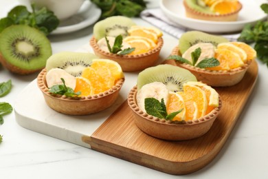 Photo of Tartlets with fruits and mint on white table, closeup. Delicious dessert