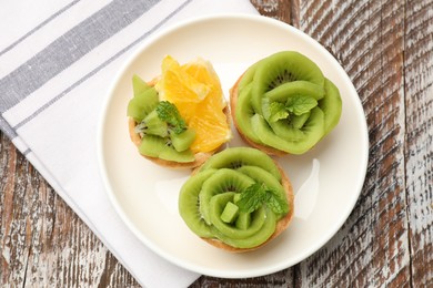 Photo of Tartlets with fruits and mint on wooden table, top view. Delicious dessert