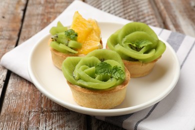Photo of Tartlets with fruits and mint on wooden table, closeup. Delicious dessert