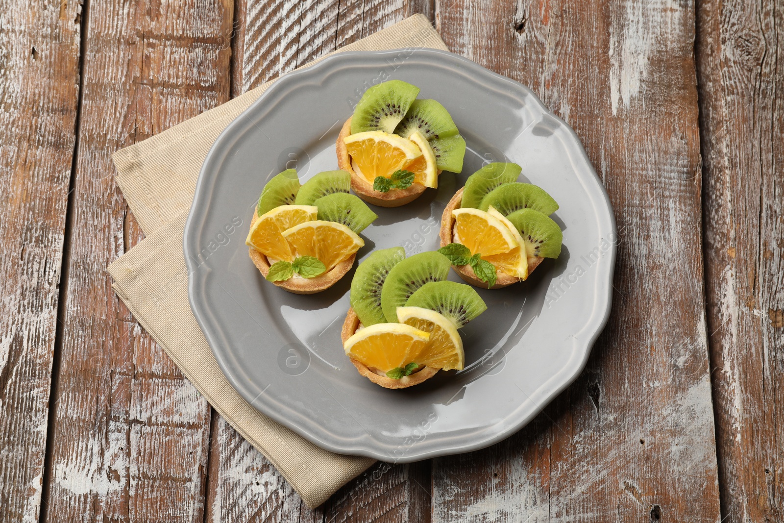 Tartlets with fruits and mint on wooden table, top view. Delicious dessert Photo of Tartlets with fruits and mint on wooden table, top view. Delicious dessert