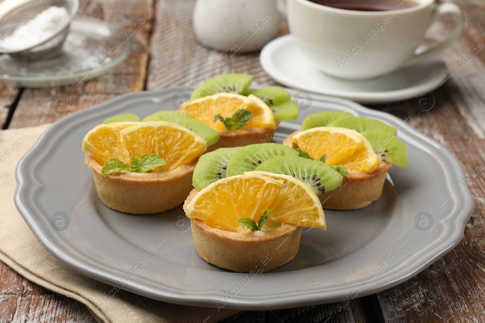 Tartlets with fruits and mint on wooden table, closeup. Delicious dessert Photo of Tartlets with fruits and mint on wooden table, closeup. Delicious dessert
