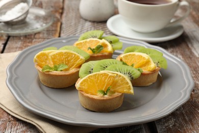 Photo of Tartlets with fruits and mint on wooden table, closeup. Delicious dessert