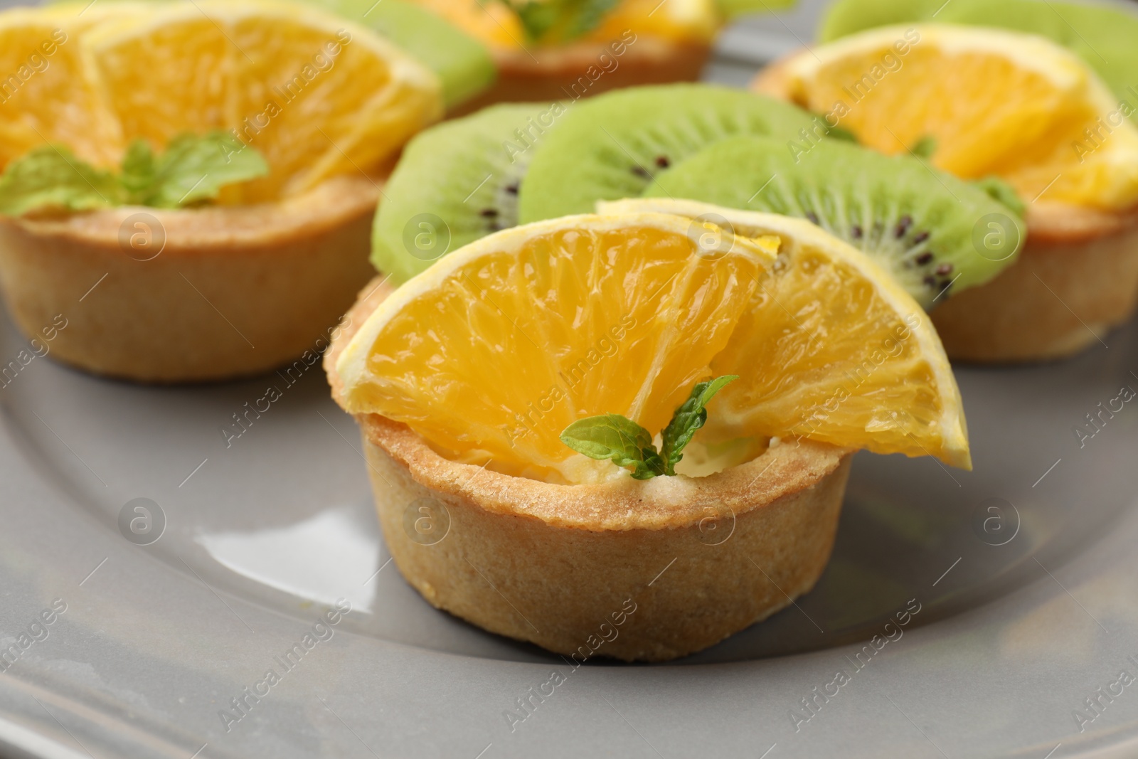 Tartlets with fruits and mint on gray plate, closeup. Delicious dessert Photo of Tartlets with fruits and mint on gray plate, closeup. Delicious dessert