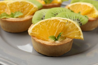Photo of Tartlets with fruits and mint on gray plate, closeup. Delicious dessert