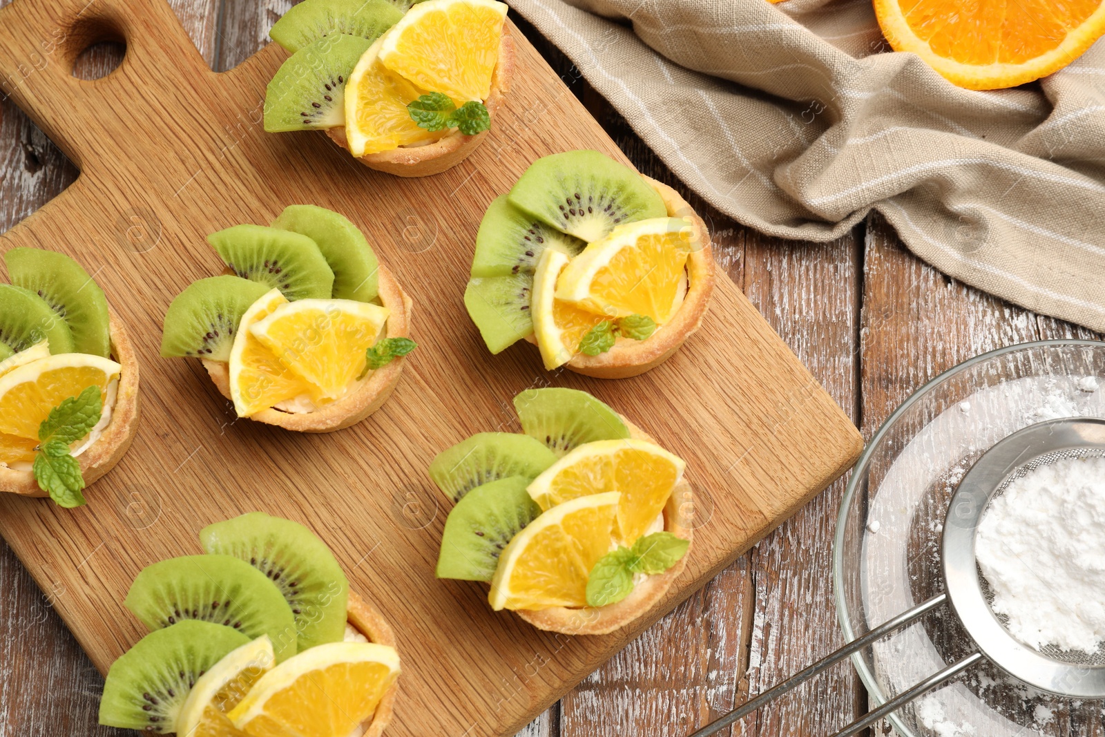 Tartlets with fruits, mint and powdered sugar on wooden table, flat lay. Delicious dessert Photo of Tartlets with fruits, mint and powdered sugar on wooden table, flat lay. Delicious dessert