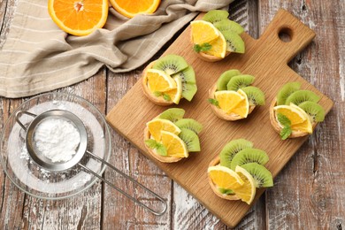 Photo of Tartlets with fruits, mint and powdered sugar on wooden table, flat lay. Delicious dessert