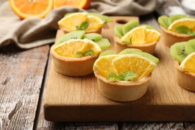 Photo of Tartlets with fruits and mint on wooden table, closeup. Delicious dessert