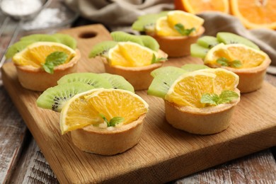 Photo of Tartlets with fruits and mint on wooden table, closeup. Delicious dessert