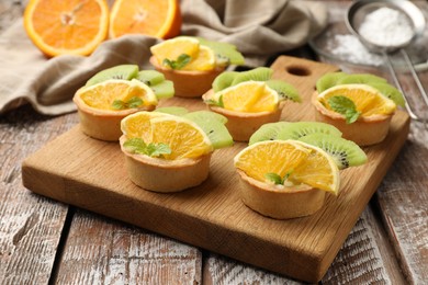Photo of Tartlets with fruits and mint on wooden table, closeup. Delicious dessert