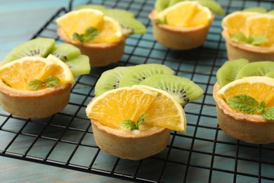 Photo of Tartlets with fruits and mint on light blue wooden table, closeup. Delicious dessert