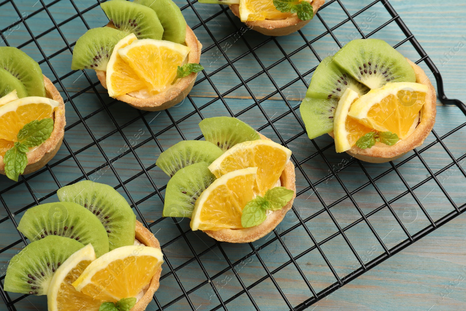 Photo of Tartlets with fruits and mint on light blue wooden table, top view. Delicious dessert