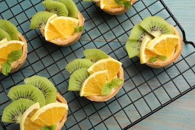 Photo of Tartlets with fruits and mint on light blue wooden table, top view. Delicious dessert